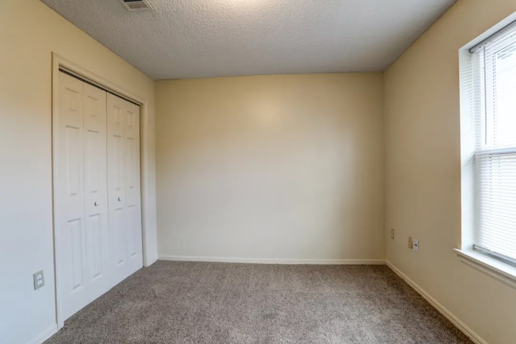 A room with a carpeted floor, a white door, and a window with blinds.